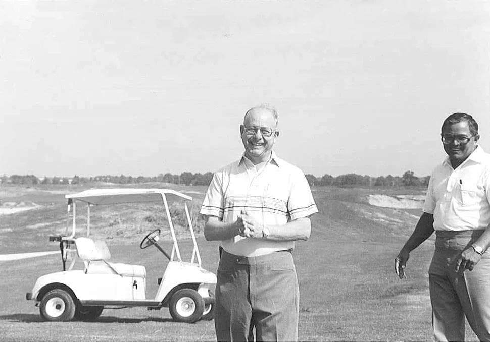 Sam Rodgers on a golf course under construction, standing beside a cart