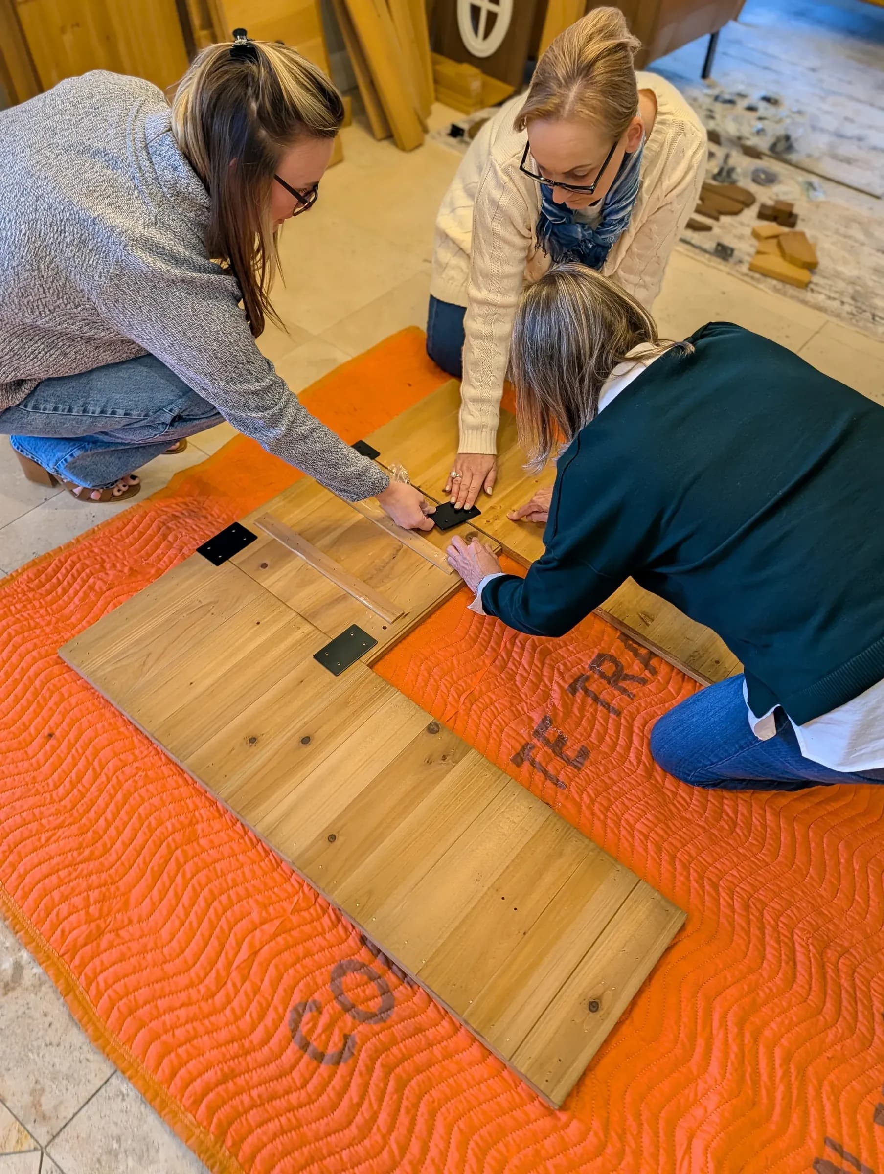 Three of the team kneeling on a moving blanket, screwing the first panel together.