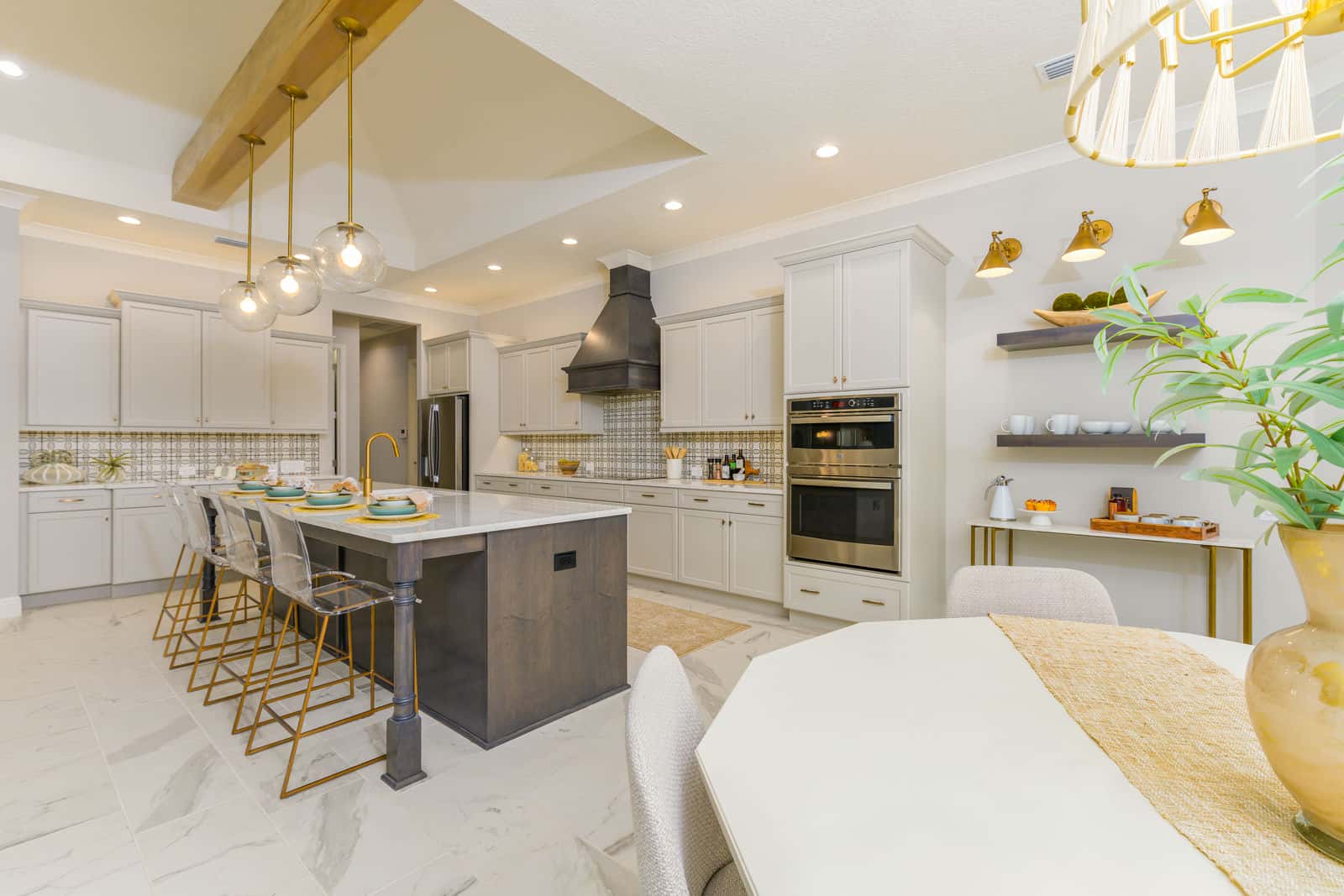 The kitchen of a Sam Rodgers Edgewater — island seating, wall ovens and a vented hood under a beamed ceiling